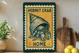 A framed illustration of a hermit crab is displayed on a shelf, accompanied by a wooden cutting board and a potted plant.