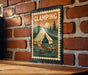A vintage-style metal sign with a camping scene, featuring a tent, chair, and table, is mounted on a brick wall.
