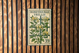 A metal sign with a floral design and the text "HONEY SUCKLE TRELLIS" is mounted on a wooden wall.