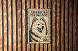 A wooden wall with a vintage-style American Eskimo dog postage stamp displayed on it.