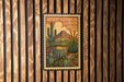 A vintage-style poster of a desert garden with cacti and other desert plants, displayed on a wooden wall.