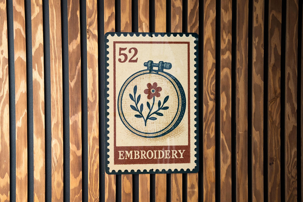 a vintage-style stamp or sign with the word "EMBROYERY" printed on it, mounted on a wooden wall.