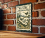 A nature-themed metal sign is displayed on a brick wall, featuring an open book with butterflies and plants, and the text "NATURE JOURNALING" on the sign.