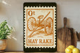 a vintage-style stamp with an illustration of a horse-drawn carriage, placed on a shelf next to a wooden cutting board and some lemons.