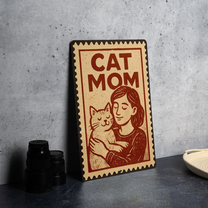 A metal sign with a woman hugging a cat, accompanied by the text "CAT MOM".