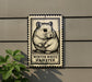 A metal sign featuring a hamster illustration is mounted on a wall, with a plant visible to the left.