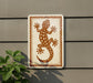 a sign with a lizard design on it, mounted on a wall next to a plant.