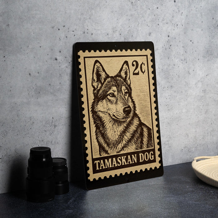 A metal stamp featuring a close-up of a dog's face, with the text "TAMASKAN DOG" printed on it.