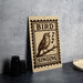 A wooden sign with a bird perched on a branch, singing, is displayed on a table next to some black camera lenses.