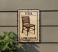 a cane chair sign mounted on a wall, with a plant to the left of the sign.