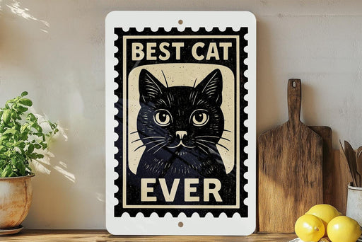 A framed sign with a black cat illustration and the text "BEST CAT EVER" is displayed on a shelf next to a wooden cutting board and a potted plant.