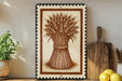 a framed illustration of a wheat stalk on a shelf, with a wooden cutting board and a potted plant to the side.