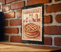 A metal sign with a farmhouse pie illustration is mounted on a brick wall.