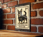 A metal sign featuring a black and tan illustration of a Lancashire Heeler dog, mounted on a brick wall.
