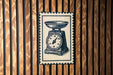 A vintage-style postage stamp featuring a scale illustration is displayed on a wooden wall.