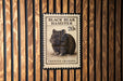 A black bear hamster postage stamp is displayed on a wooden wall.