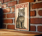 A framed illustration of a bobcat is displayed on a brick wall.