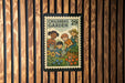 A children's garden stamp with illustrations of children working in a garden, displayed on a wooden wall.