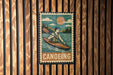 A vintage-style metal sign with a canoe and the word "Canoeing" written on it, mounted on a wooden wall.