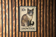 A 10c postage stamp featuring a Siamese cat is displayed on a wooden wall.