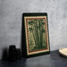 a framed print of bamboo plants on a wall, with a black border and a red border. There are also some black camera lenses and a white dish on a countertop.