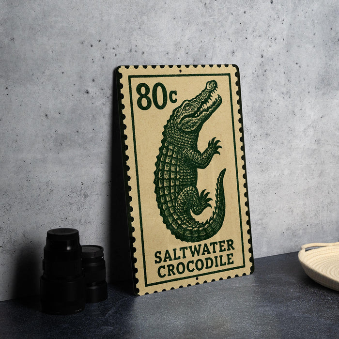 A saltwater crocodile postage stamp is displayed on a table, with a stack of black camera lenses and a white plate nearby.