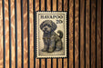 A small, fluffy dog is depicted on a postage stamp, which is affixed to a wooden wall.