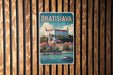 A vintage-style metal sign with the text "BRATISLAVA" and an illustration of a castle on a hill overlooking a river.