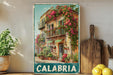 A vintage-style metal sign with a colorful illustration of a building with flowers on the balcony, surrounded by potted plants, placed on a wooden shelf next to a cutting board and some lemons.