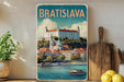 A vintage-style metal sign with the text "BRATISLAVA" and an illustration of a castle overlooking a river, surrounded by buildings and boats.