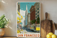 A framed poster of a street scene in San Francisco, featuring a trolley car and colorful buildings, is displayed on a shelf next to a wooden cutting board and some potted plants.