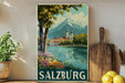 A framed vintage-style poster of Salzburg, Austria, depicting a scenic view of the city with a mountain in the background and a river in the foreground.