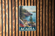 A vintage-style metal sign with a scenic image of a rocky coastline and a lighthouse, mounted on a wooden wall.