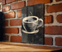 A black and white illustration of a coffee cup is displayed on a brick wall, mounted on a wooden surface.