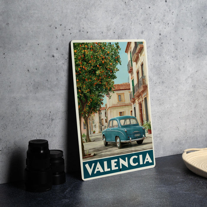 A vintage-style photograph of a blue car parked on a street in a Spanish town, with a tree and buildings in the background.