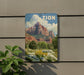 A vintage-style sign with a mountain landscape and colorful flowers is displayed on a wall, with a plant to the left.