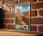 A vintage-style metal sign with a scenic image of Bryce Canyon National Park, featuring towering red rock formations and a blue sky with clouds.