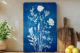 a blue floral print on a wooden surface, with a wooden cutting board and a potted plant to the left.