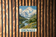 A vintage-style poster of a mountain landscape with a river and flowers is displayed on a wooden wall.