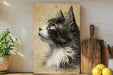 A framed black and white drawing of a cat's profile is displayed on a shelf, accompanied by a potted plant, a wooden cutting board, and a bunch of lemons.