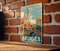 A vintage-style metal sign displaying the image of the city of Bruges, Belgium, with a church spire and a bridge in the background.