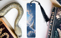 a bookmark with a picture of a snake and clouds on it, placed on a white surface next to a book and a decorative snake.