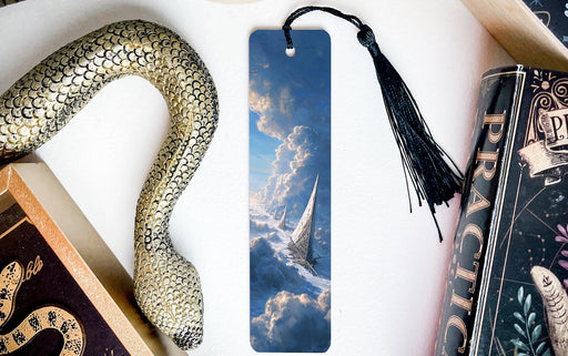 a bookmark with a picture of a snake and clouds on it, placed on a white surface next to a book and a decorative snake.