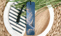 A bookmark with a picture of a sailboat on a cloudy sky is placed on a plate with a striped pattern.