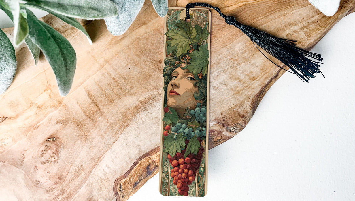 A wooden bookmark with a decorative design featuring a woman's face surrounded by grapes and leaves.