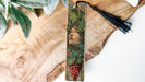 A wooden bookmark with a decorative design featuring a woman's face surrounded by grapes and leaves.