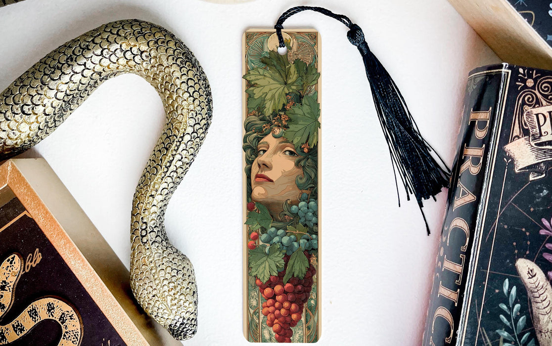 a decorative bookmark with a snake design and a woman's face on it, placed on a white surface next to a book.