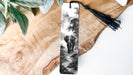 A black and white photograph of an elephant walking through a forest, displayed on a wooden surface with a black tassel hanging from the top.