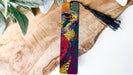 A colorful, abstract bird-like design on a bookmark, with a black tassel hanging from the top.