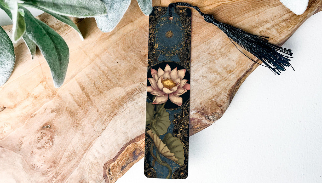 A decorative bookmark featuring a pink lotus flower and green leaves rests on a wooden surface, accompanied by a black tassel.
